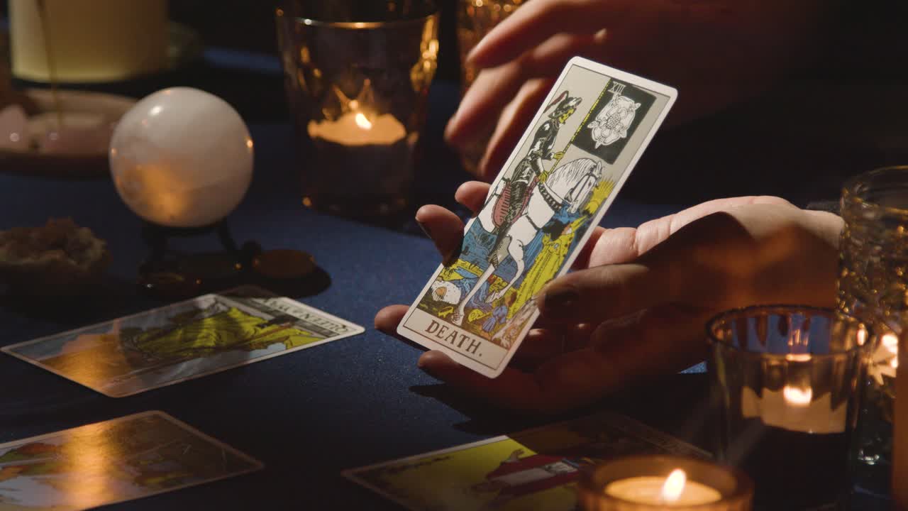 primer plano de una mujer dando una lectura de tarot en una mesa a la luz de las velas sosteniendo la carta de la muerte 1