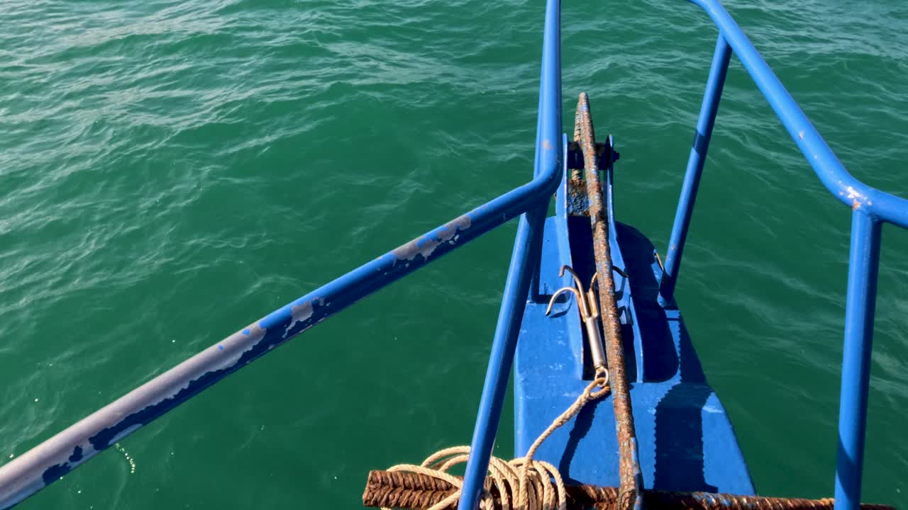 A fishing boat glides over calm, emerald waters in Phuket, Thailand. Bright sunlight enhances the vibrant blue and green hues