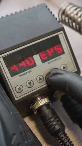 vista de cerca de una mano con guante ajustando el control digital de la temperatura en una estación de soldadura, de 234 grados a 244 grados y de vuelta a 243 grados