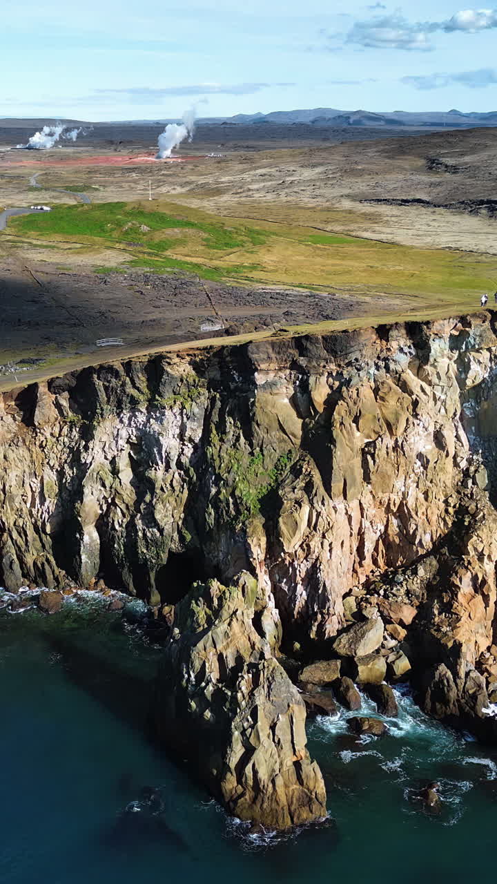 Aerial drone view of dramatic sea cliffs rising above the North Atlantic Ocean. Steep volcanic rock formations drop into deep blue water along Iceland's rugged coastline. Vertical