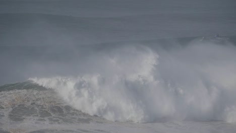 rough ocean wave crashing at praia de nazaré, portugal, with a misty atmosphere