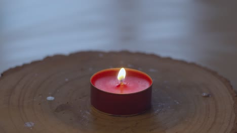 red candle, sitting on a wooden plank, being lit and burning