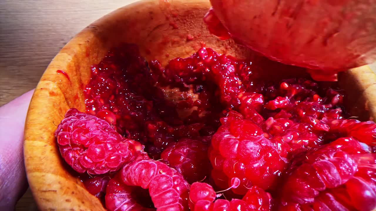 Crushing fresh raspberries with a wooden pestle, vibrant and juicy