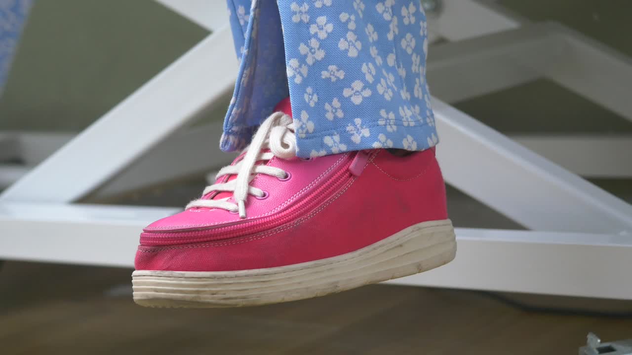 Woman's feet in pink shoes and light blue pants sitting on an adjustable height chair