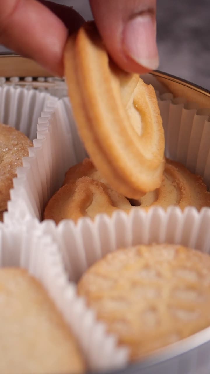 Hand Picking Up a Golden Butter Cookie from a Decorative Tin