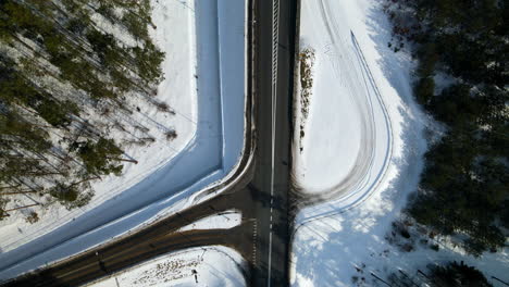 drone over black road near forest during snowy winter, moderate traffic, top down, poland