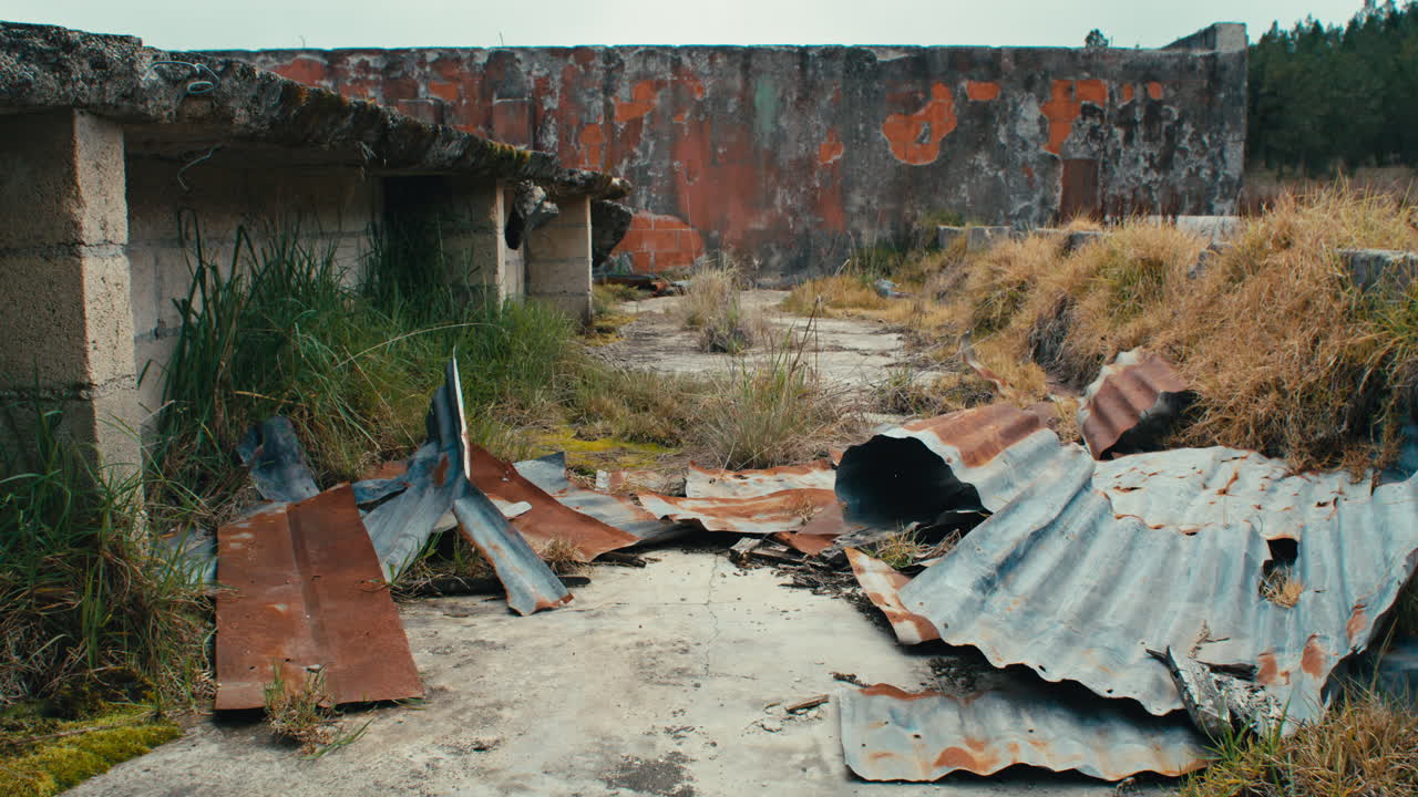 hojas de techo de zinc oxidadas en el suelo fuera de la estructura de cemento abandonada en un campo de hierba de tussock dentada disparo de detalle estático
