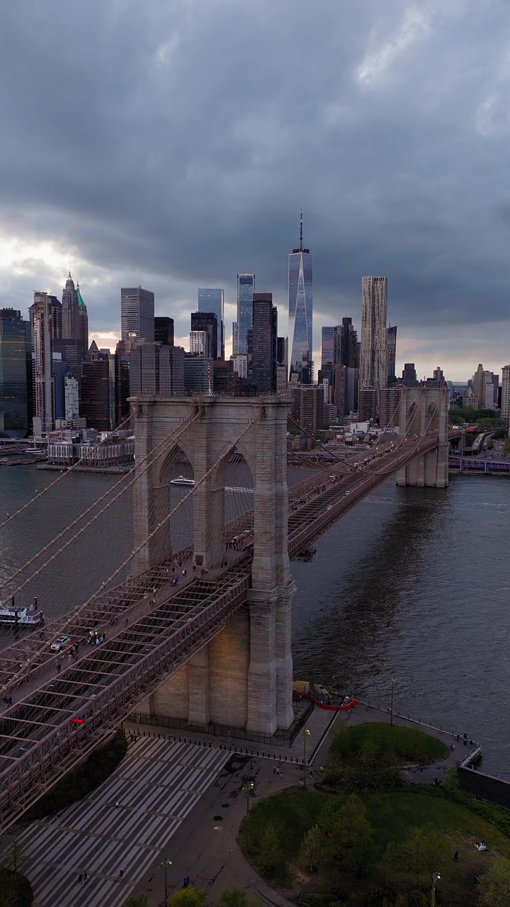 Ripresa panoramica verticale con drone del Ponte di Brooklyn al tramonto, New York City. Bandiera americana visibile in cima alla torre. Skyline di Manhattan, One World Trade Center sullo sfondo. Filmato aereo.