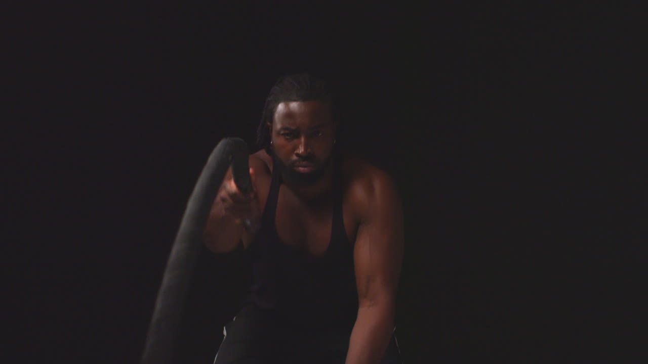 toma de estudio de un atleta masculino entrenando usando un chaleco usando cuerdas de batalla tomada contra un fondo negro
