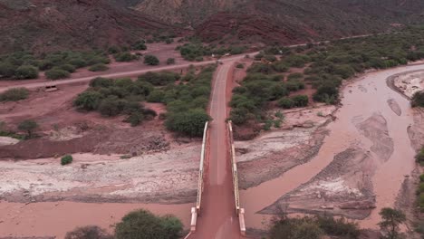 un camino de tierra roja y un puente que cruza un lecho de río seco en la ruta 68, salta, argentina, vista aérea