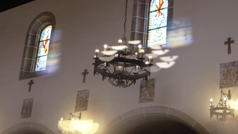 sunlight casts vivid colors through stained glass windows onto church walls and chandelier
