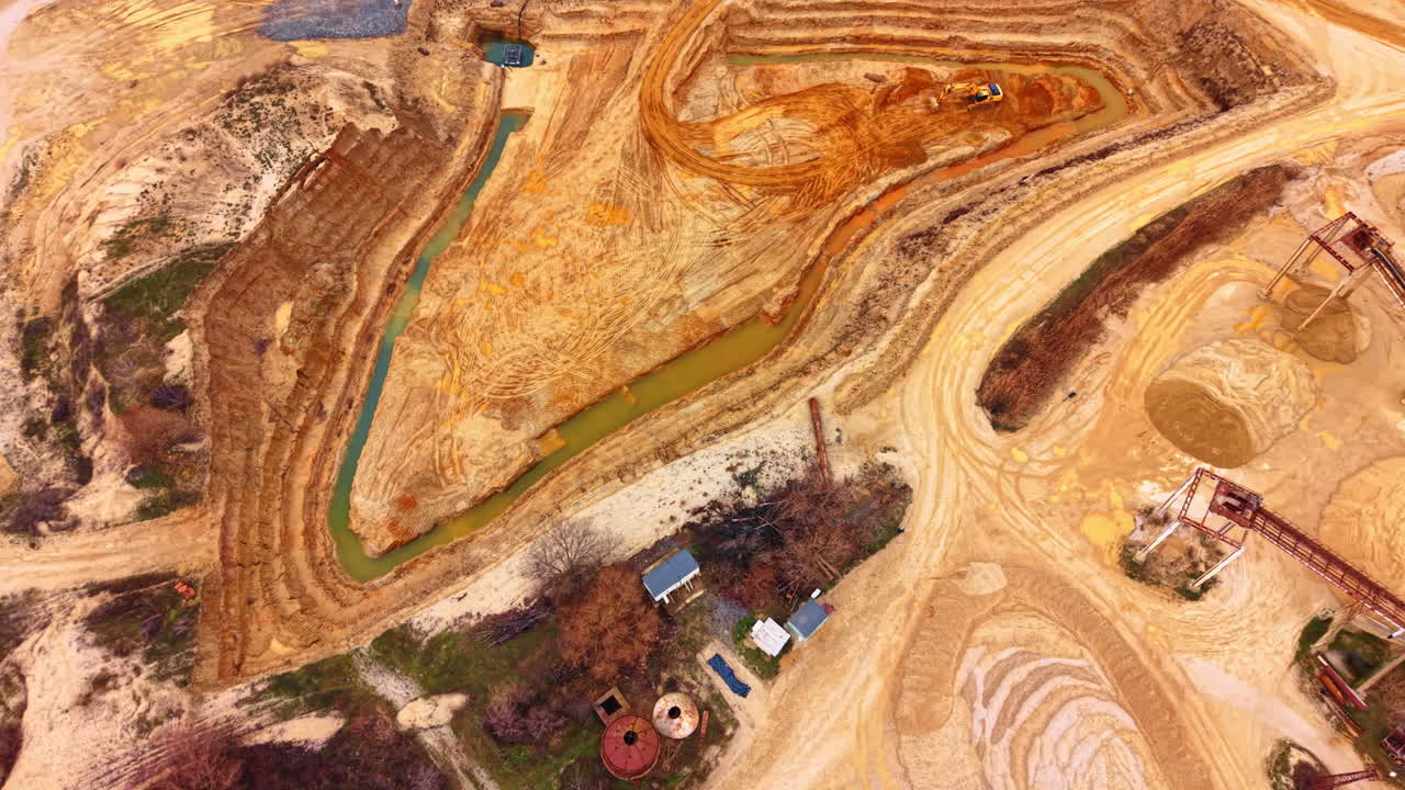 Aerial view of open pit sand quarry with water trench. High angle drone shot of industrial sand excavation site with orange soil and narrow green water channel