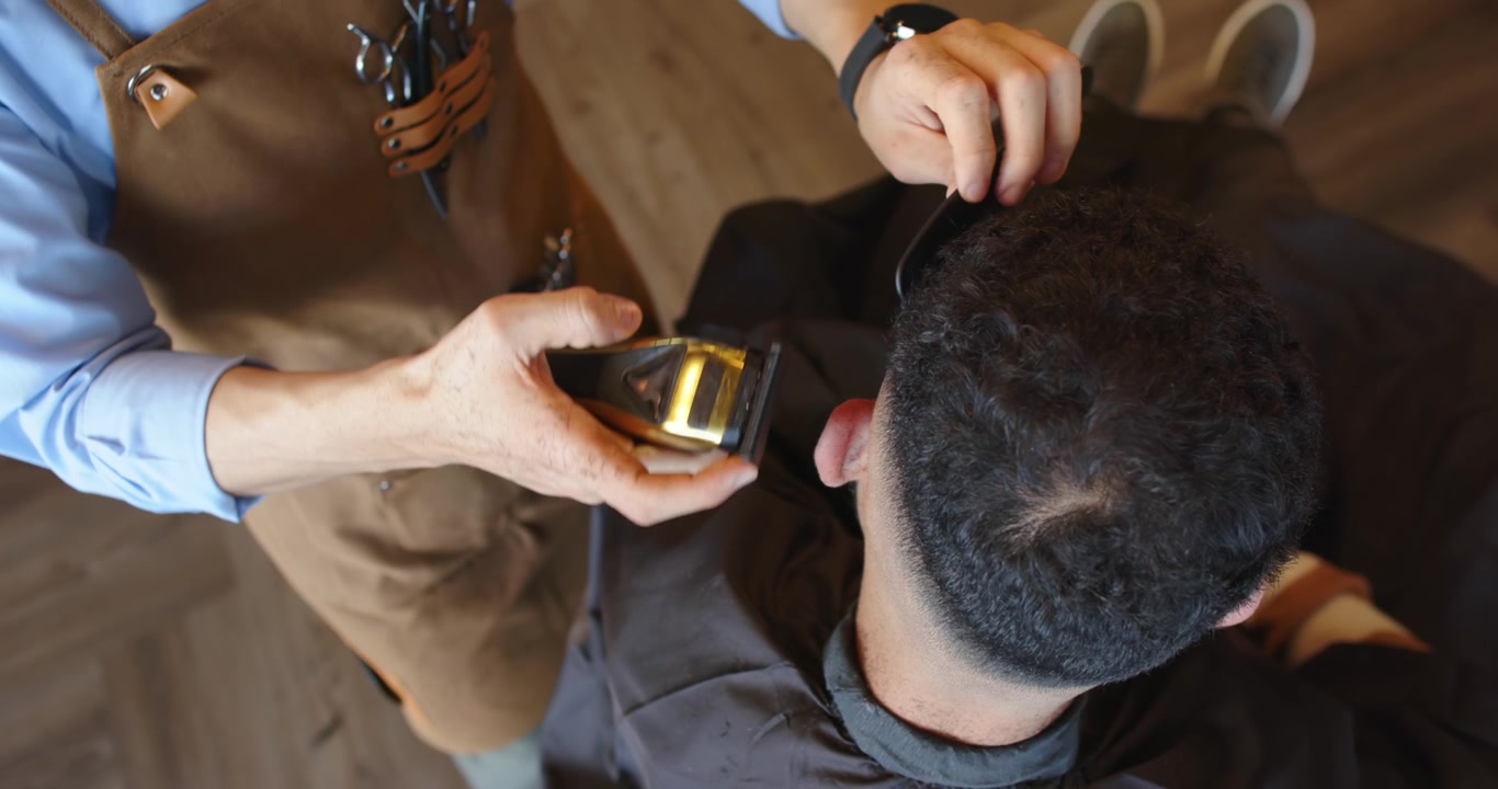 Afrikansk mandlig barber klipper kunde, placerer guldtrimmer nær venstre øre og forfiner fade-klipningen i barbersalonen.