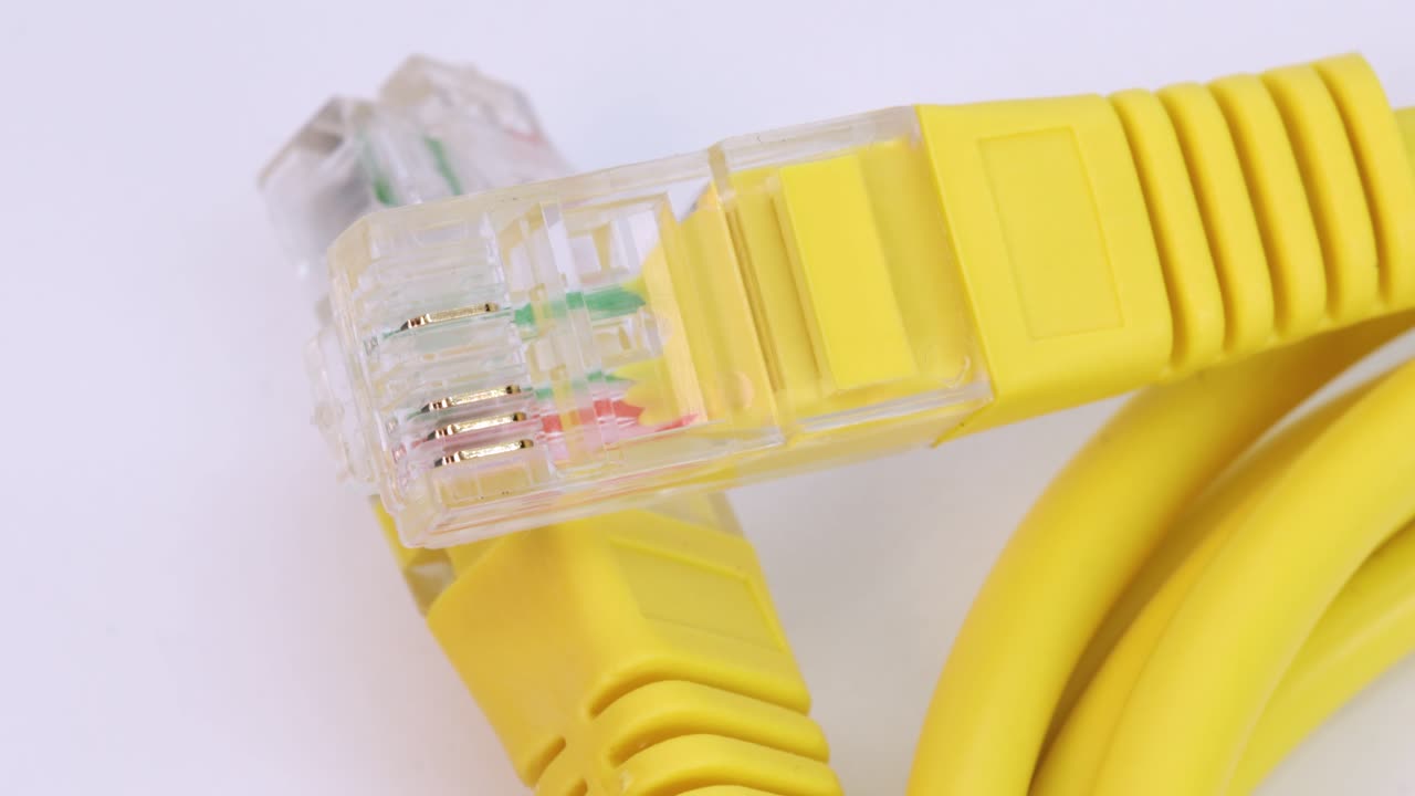 Macro shot of ethernet cable of yellow plastic rotating on white surface, close up view from above in 4k