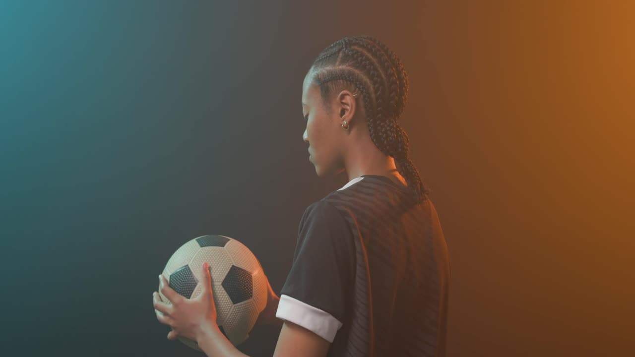 African American woman cradling soccer ball in dark jersey preparing for game in studio, copy space