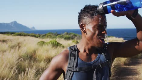 African american man exercising outdoors drinking water in countryside on a coast
