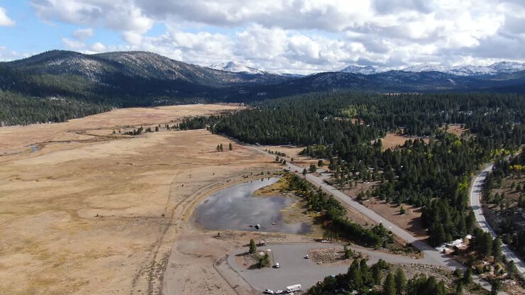 Video panoramico aereo di una strada divisa in due, un bellissimo lago riflettente e cime innevate sullo sfondo, girato a Lake Tahoe, Sierra Nevada, California