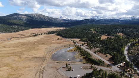 Aerial-panoramic-video-of-a-split-in-two-road,-a-beautiful-reflective-lake,-and-snowy-peaks-in-the-backshoot-in-Lake-Tahoe,-Sierra-Nevada,-California