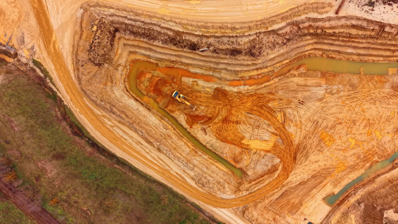 Draufsicht auf Bagger, der in einer Sandgrube arbeitet. Vertikale Luftaufnahme eines gelben Hydraulikbaggers, der in orangefarbenem Sand einen Graben mit Wasserkanal aushebt.
