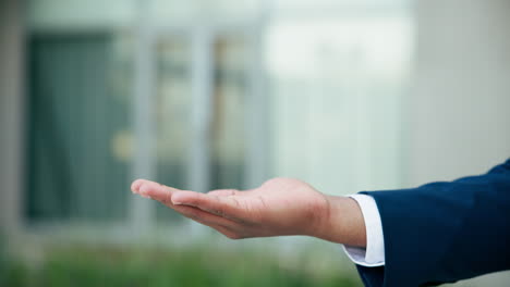 businessman's open hand gesture in front of a building