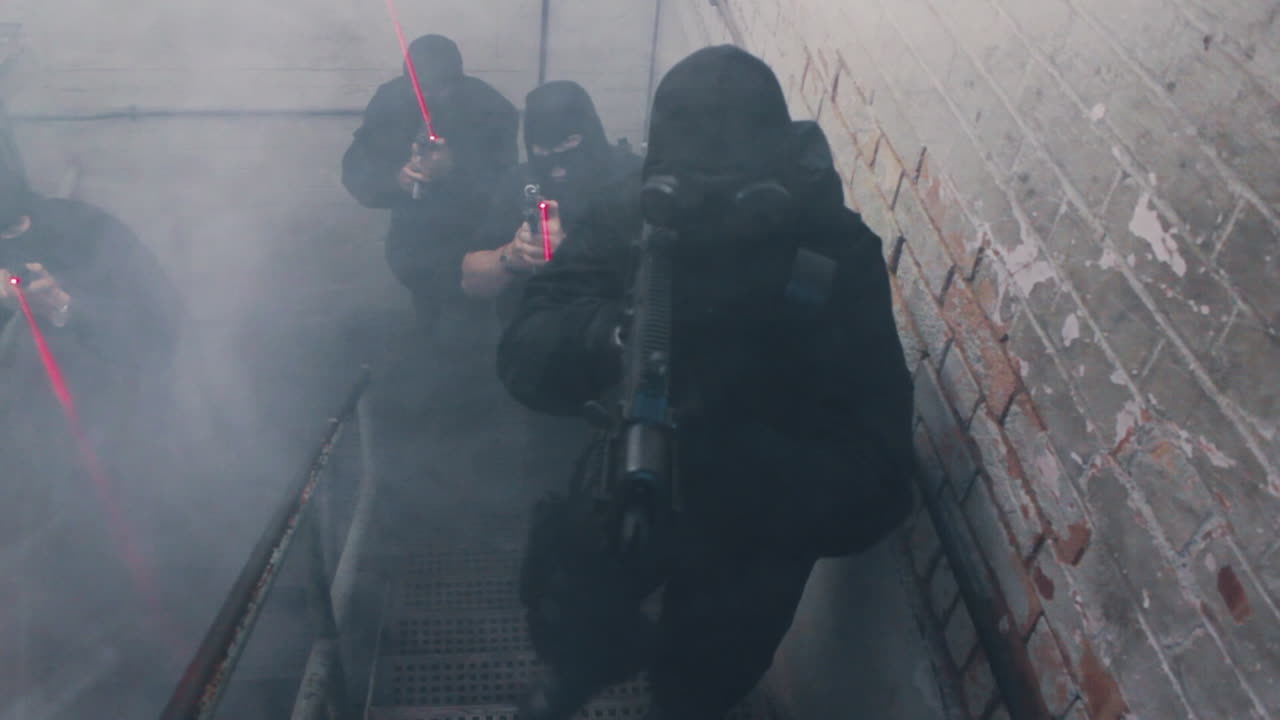 A special forces swat team ascends a stairwell with guns and laser sights wearing balaclavas and gas masks