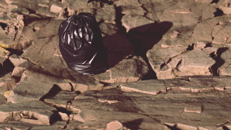 black trash bag lay on a rocky beach