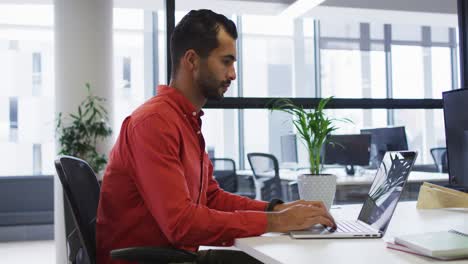 Mixed-race-businessman-sitting-at-desk-using-laptop