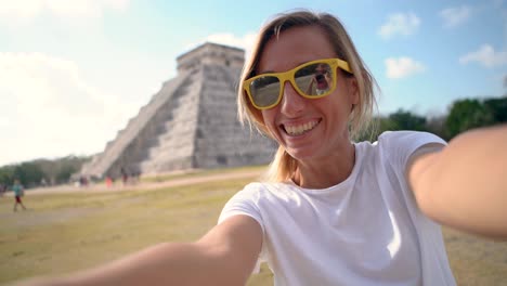 cute blond woman taking selfie video in front of ancient mayan temple in mexico. girl on vacations making video chat on mobile phone white sightseeing in central america