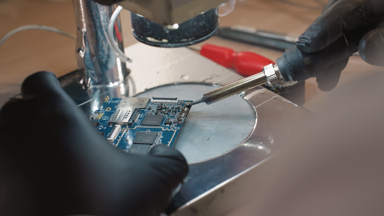 A close-up view of a technician hand soldering a printed circuit board PCB with a soldering iron in an electronic repair workshop with other tools close by