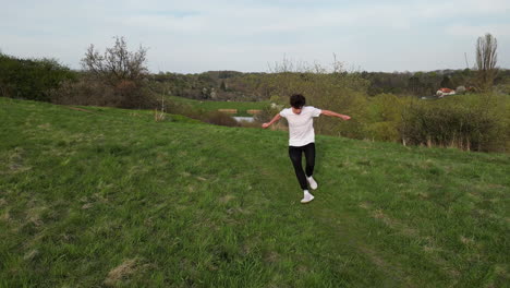 aerial view of young man doing somersault roll and running in green outdoor field, slow motion drone shot