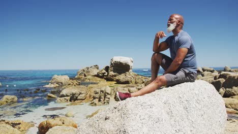 hombre afroamericano de alto nivel haciendo ejercicio sentado en rocas junto al mar