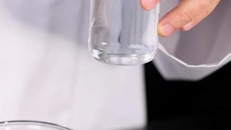 a person in a lab coat pours liquid from a bottle into a glass beaker.
