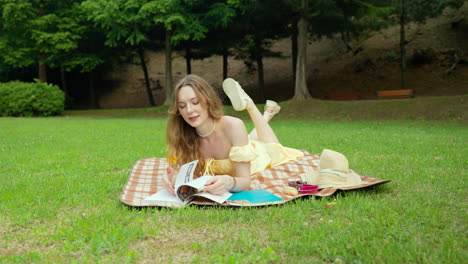 woman resting face in hand, lying on stomach, looking through book, feet in air