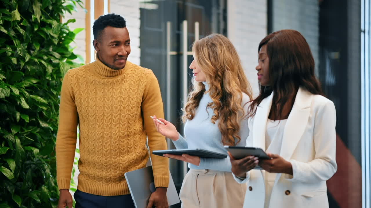 Multiracial group of workers walking in an office and discussing business affairs using tablets. Slow motion