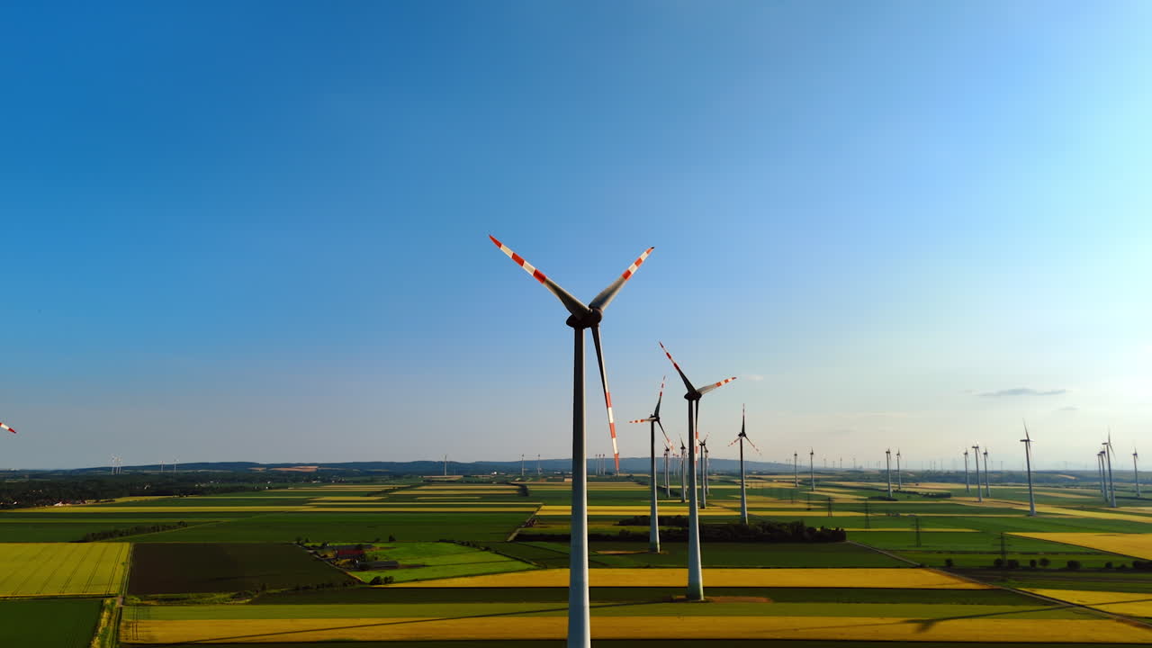 Turbines create renewable energy. Vast green fields dotted with wind turbines stretch under a clear blue sky, showcasing renewable energy production