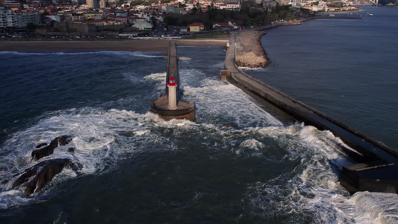 Drone spiral descend capturing slow motion dramatic wave action at Porto's Forte de São João breakwater where Atlantic waters crash against Felgueiras Lighthouse beacon stands sentinel, Portugal