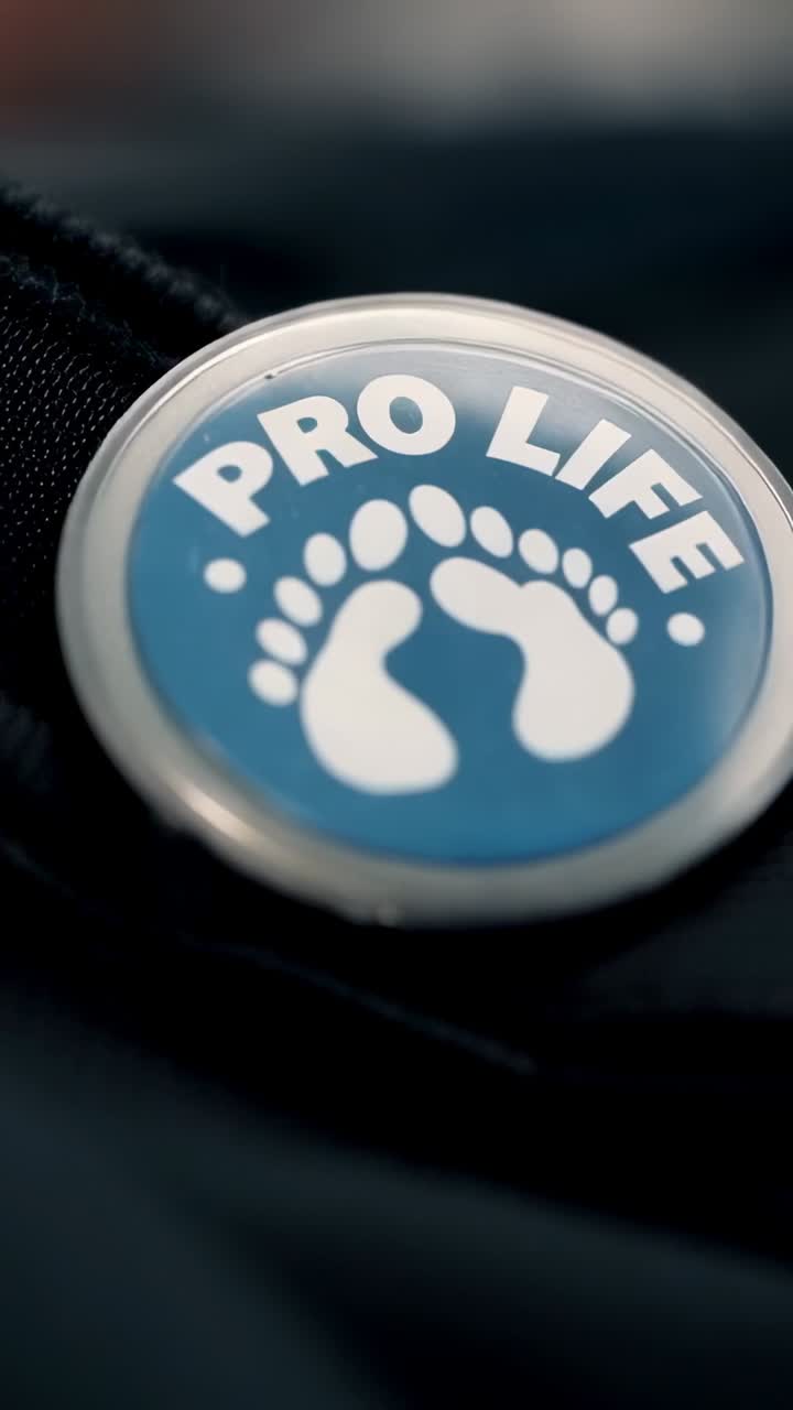 Vertical video: Zooming in, camera revealing PRO LIFE pin on jacket to reveal text and footprints