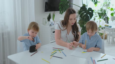 Two-children-of-boys-draw-with-his-mother-sitting-in-the-kitchen.-Happy-family-at-home.-Brothers-draw-at-the-table.-Real-people.