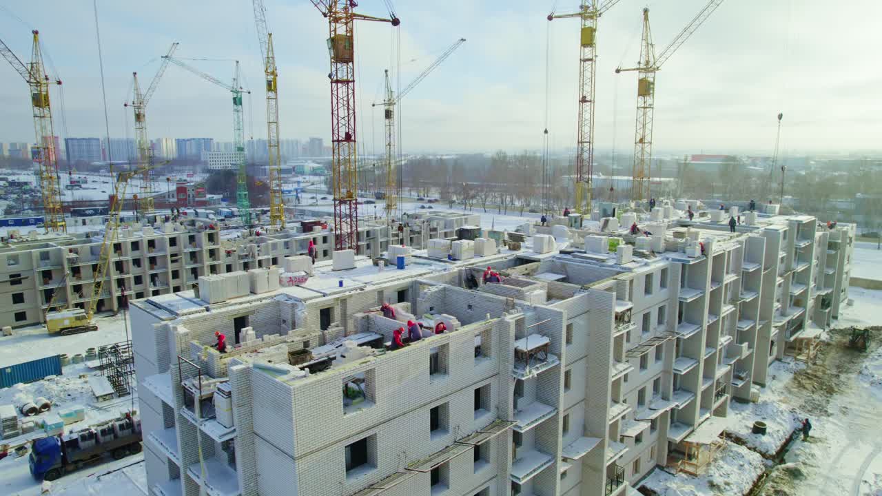 Construction site with workers building residential apartments under cranes in winter
