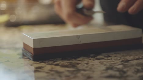 Mano-De-Una-Persona-Afilando-Un-Cuchillo-Pequeño-En-Una-Piedra-De-Afilar