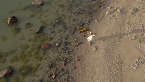 View-from-above-of-woman-in-a-dress-at-a-lonely-beach-in-morning-sunrise