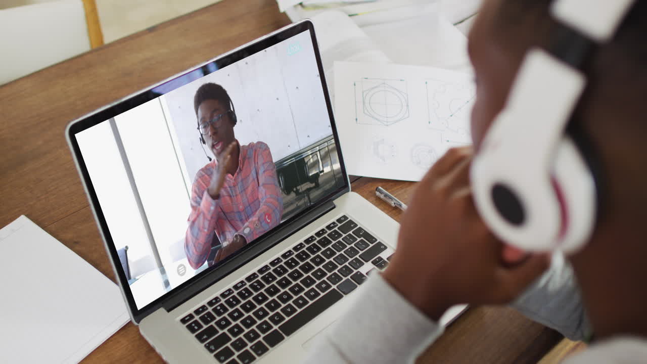 African american male college student wearing headphones having a video call on laptop at home