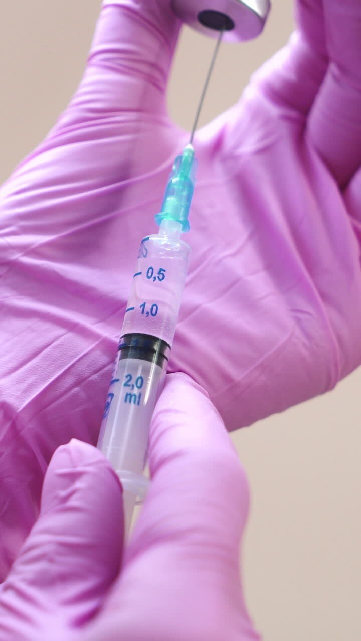 Close-up view on a cosmetologists hands in gloves holding syringe with needle for rejuvenating facial injections. Vertical video