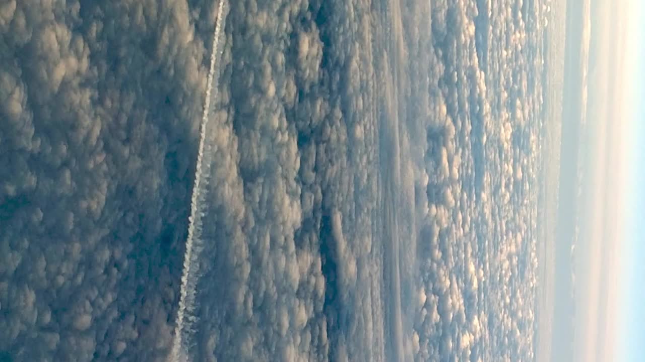 Uncommon view from cockpit of flying airplane above clouds leaving long white condensation vapor air trail in blue sky
