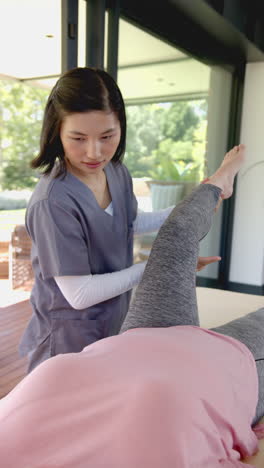 vertical video: physiotherapist assisting senior patient with leg exercise during home visit