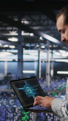 Vertical video Technician holding laptop walking on server farm platform