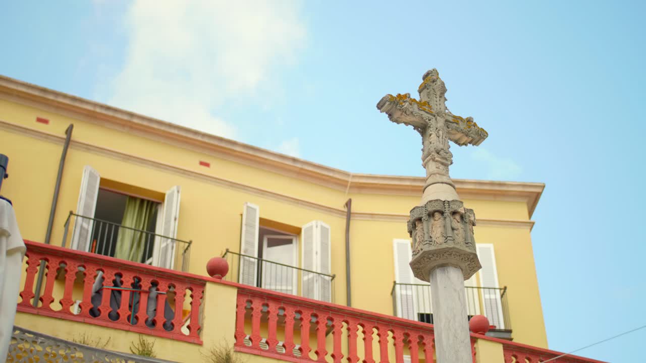 cruz antigua e histórica frente a la arquitectura española con cielo azul en segundo plano.