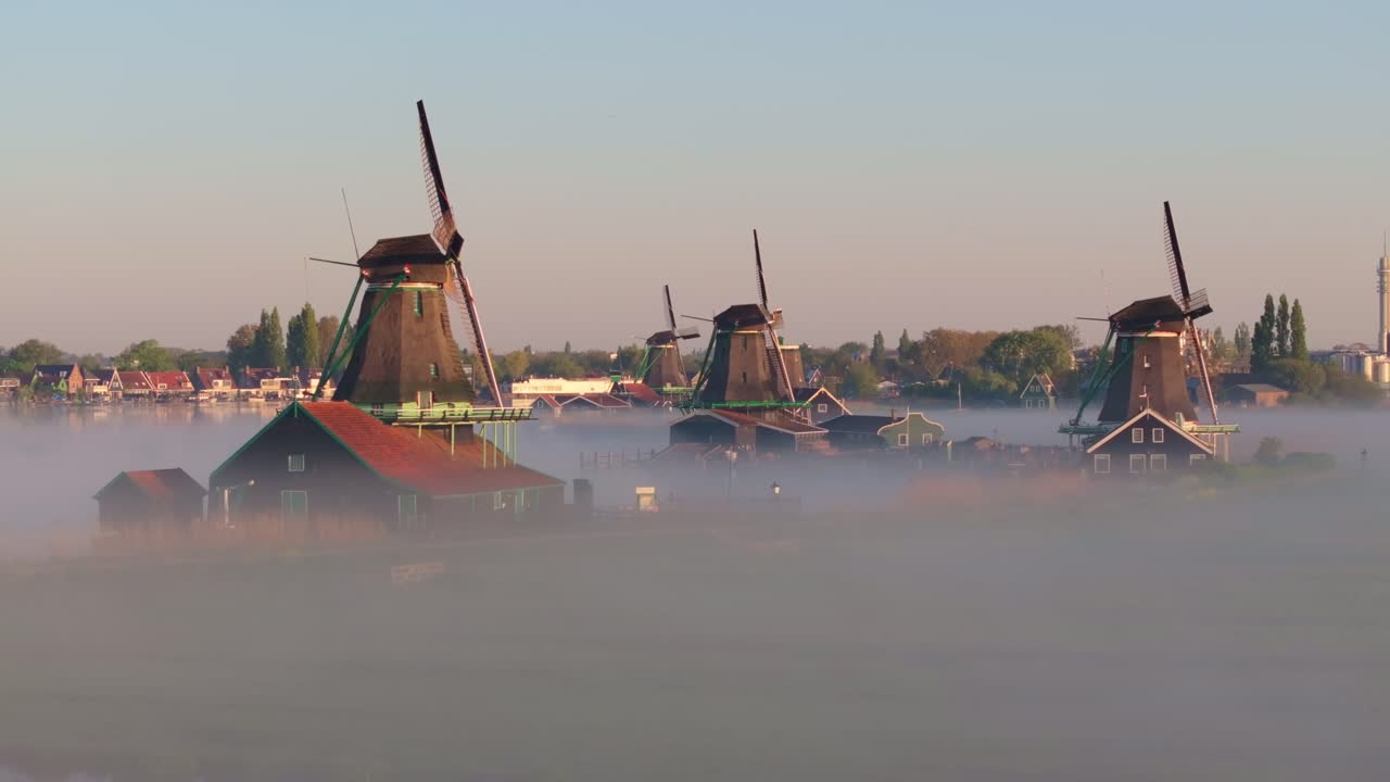 Luftaufnahme von Windmühlen am Kanal, die im nebligen Sonnenaufgang leuchten, Niederlande.