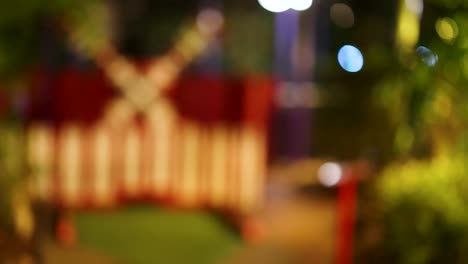 blurred view of a mini golf course with a windmill, colorful lights, and greenery, creating a dreamy nighttime atmosphere