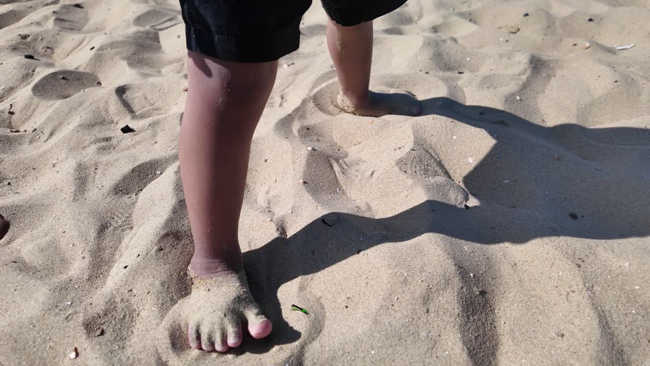 Close up of child's feet sinking into warm beach sand, creating footprints on a sunny summer day